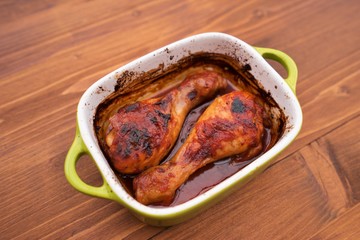 Chicken drumsticks marinated in soya sauce, honey, beer and tomatoes and than roasted in small ceramic roasting pan. Close up Picture served in the pan without any side dish or salad. 
