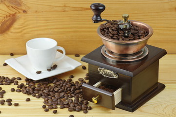 Old-style manual coffee grinder on a rustic table with wooden planks. Around the mill are scattered...