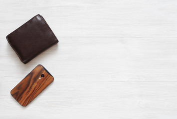 Braun leather wallet and and mobile phone on wooden white floor background, top view. 