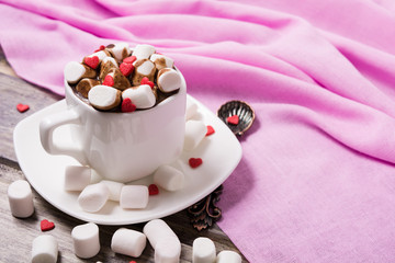 Hot chocolate in white cup with marshmallow and sweet hearts on the wooden table. Copy space
