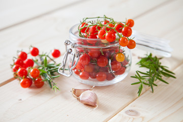 tomatoes in a jar, rosemary and garlic on a wooden background, selective focus