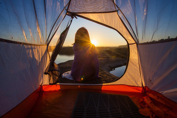 women sit front of camping tent glow up with sunrise in morning