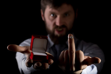 bearded man in business suit gives a ring in the red box and showing middle finger on dark background