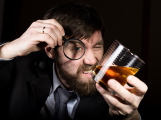 portrait of handsome young businessman looking at brandy through magnifying glass