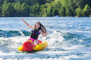 Laughing young girl speeds across a lake, hands in the air, on an inflatable on a summer day