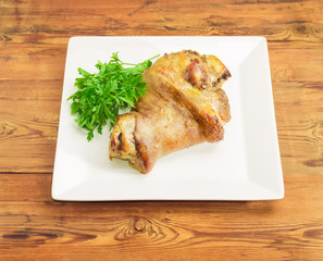 Baked ham hock on square white dish on wooden surface