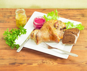 Baked ham hock with condiments on white dish and bread