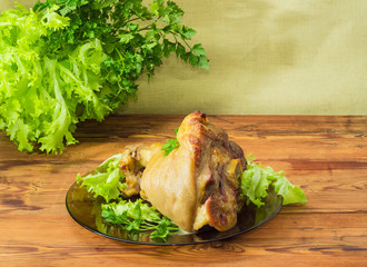 Baked ham hock on glass dish on background of greens