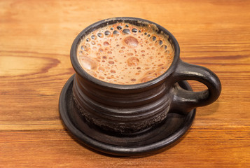 Coffee in black ceramic cup on wooden surface closeup