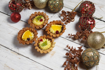 Homemade desserts with fruits for the new year. Desserts for the holidays. View from above. Christmas decorations and toys. The desserts on the wooden background.
