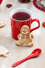 Tea, ginger man cookie and and red spoon on plywood background.