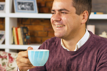 Young man holding a cup of coffee in hand and smiling.