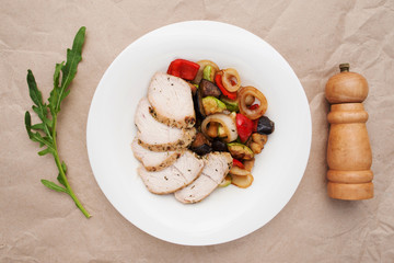 Vegetable ragout with chicken meat flat lay. Top view on beige table with hot dish of stewed vegetables ant poultry, with arugula and pepperbox. Healthy food, restaurant menu, concept