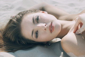  a beautiful young girl lying on the beach face close-up