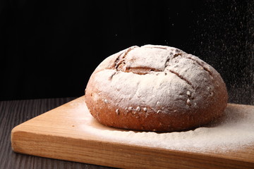 bread/ bread, flour sprinkled on an oak board on a dark background