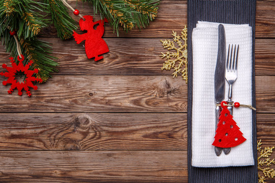 Christmas table place setting with fork and knife, decorated christmas toy - red fir-tree, gold snowflakes and christmas pine branches.