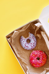 Carton box with tasty donuts on yellow background, close up view