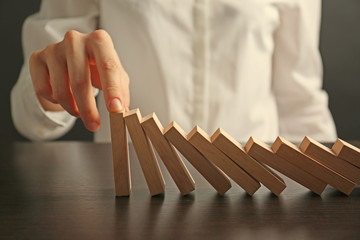 Businesswoman hand trying to stop toppling dominoes on table