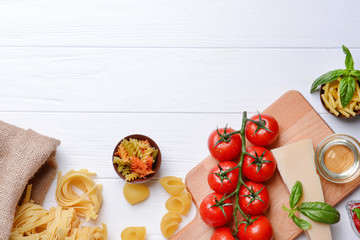 Different kinds of pasta and tomatoes on wooden background
