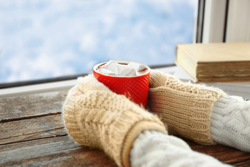 Human hands holding cup of coffee on windowsill