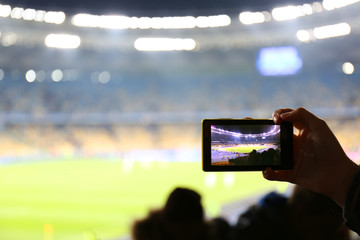 Fototapeta premium Fan taking video of football game at stadium