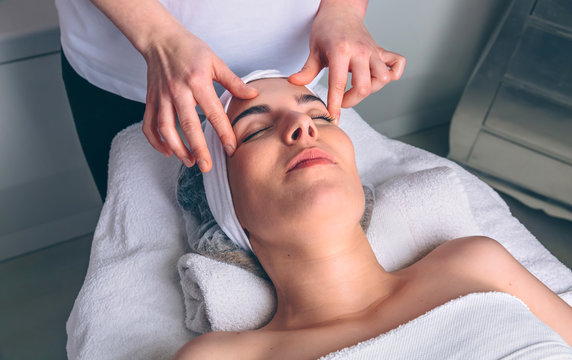 Young woman with closed eyes receiving facial massage on a clinical center. Medicine, healthcare and beauty concept.