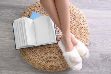 Human legs in slippers on ottoman beside open book