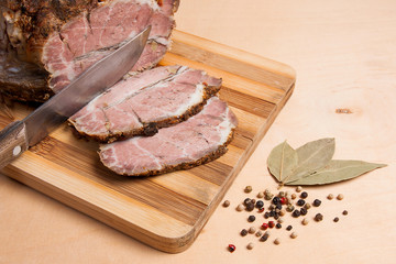 Sliced baked pork with herbs and spice on wooden board.
