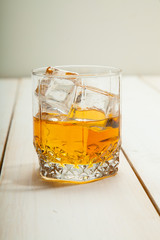 glass of whiskey with ice on a white wooden background