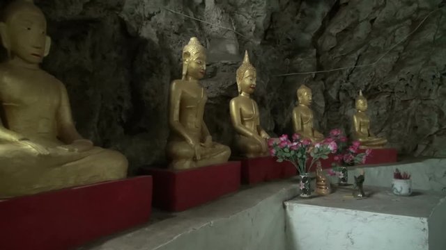 Pan left to right across a row of Buddha images. A small cave occupied by a Monk for 30yrs. Artificial lighting is not allowed. The cave is lit by a small hole in it's roof and a few recessed lights.