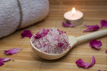 Obraz na płótnie Canvas homemade body scrub from sea salt and rose petals and peony candle,pink towel on a straw Mat. Spa concept