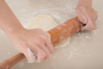 female hands rolling raw dough on white