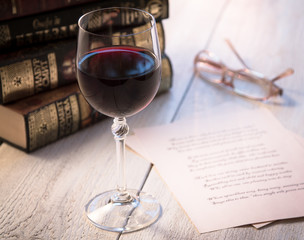 Books, a glass of wine and poetry on the old wooden table. Shakespeare Poems