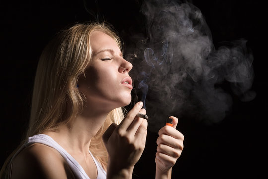 woman smoking joint of marijuana on black background