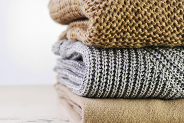 three warm sweaters are stacked on the table on a light backgrou