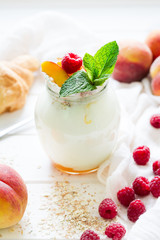 Yogurt with peach and raspberries in a glass jar on white wooden background. Selective focus