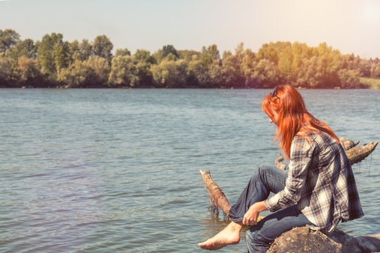 Young woman with red hair in checkered shirt and sunglasses at the river in the sunny day. Coloring and processing photo with soft focus in instagram style.