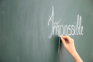 Female hand transforming IMPOSSIBLE into POSSIBLE on chalkboard