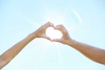 Couple making heart shape with hands on blue sky background