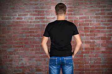 Handsome young man in blank black t-shirt standing against brick wall