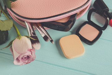 Cosmetic bag, rose and makeup products on wooden   background