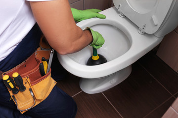 Plumber repairing toilet with hand plunger, closeup