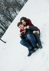 Fototapeta premium Funny man and a beautiful girl, they go from the mountain on a sled. Romantic feelings and positive emotions, joy. Scenic winter walk in Park. Fantastic shooting. Fashionable toning. Creative color.