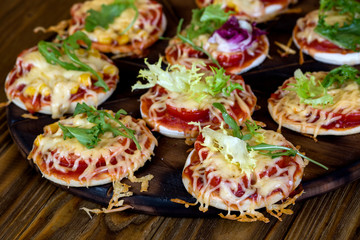 Small pizzas with mozzarella cheese, lettuce and cherry tomatoes on the baking pan
on a wooden background
