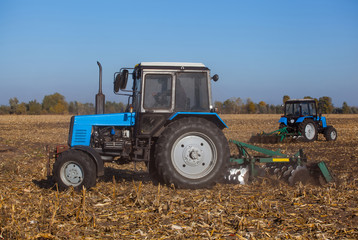 Obraz premium Two big blue tractor plowing a field and remove the remains of previously mown corn. The work of agricultural machinery. Harvest