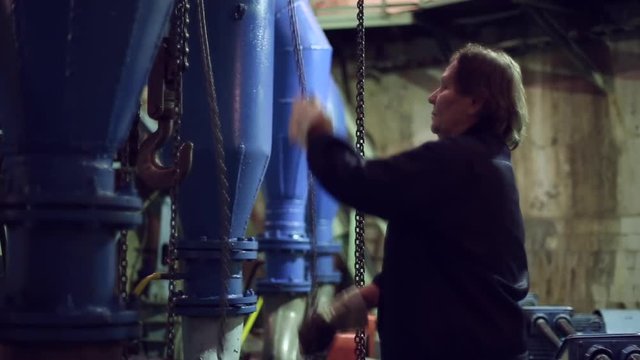Industrial round-link chains for hoists, a cargo hook on the drive chain, woman pulled the chain and move hoist on pumping station
