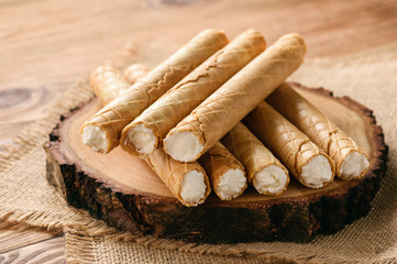 Rolled wafers with whipped cream filling on wooden background.
