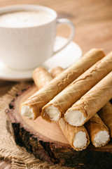 Rolled wafers with whipped cream filling on wooden background.