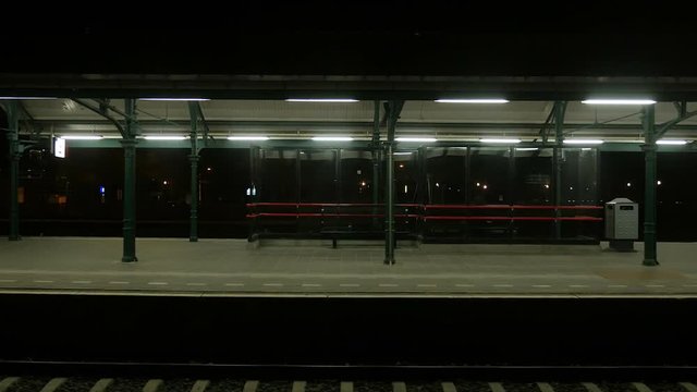 Very slowly leaving a deserted train station in the Netherlands, shot from a train. Lamps, lights, a few signs and an empty snackbar are all we see before entering darkness.