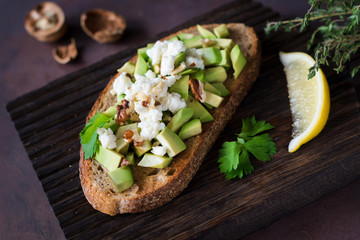 Healthy snack with avocado, white cheese, walnuts and olive oil on toasted whole grain bread. Close up view, selective focus
